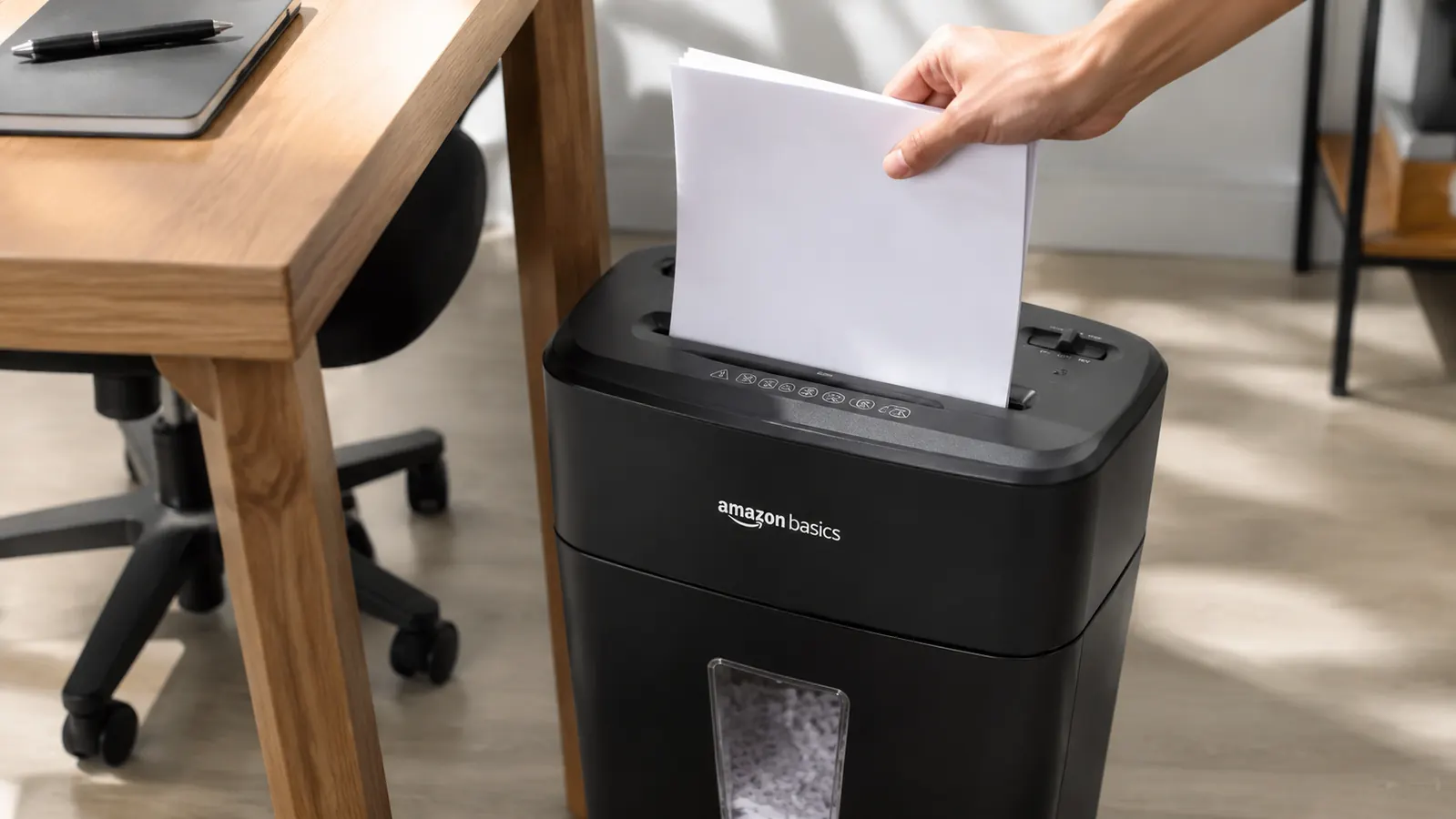Close-up of a hand feeding a stack of paper into the Amazon Basics cross-cut shredder on a home office floor