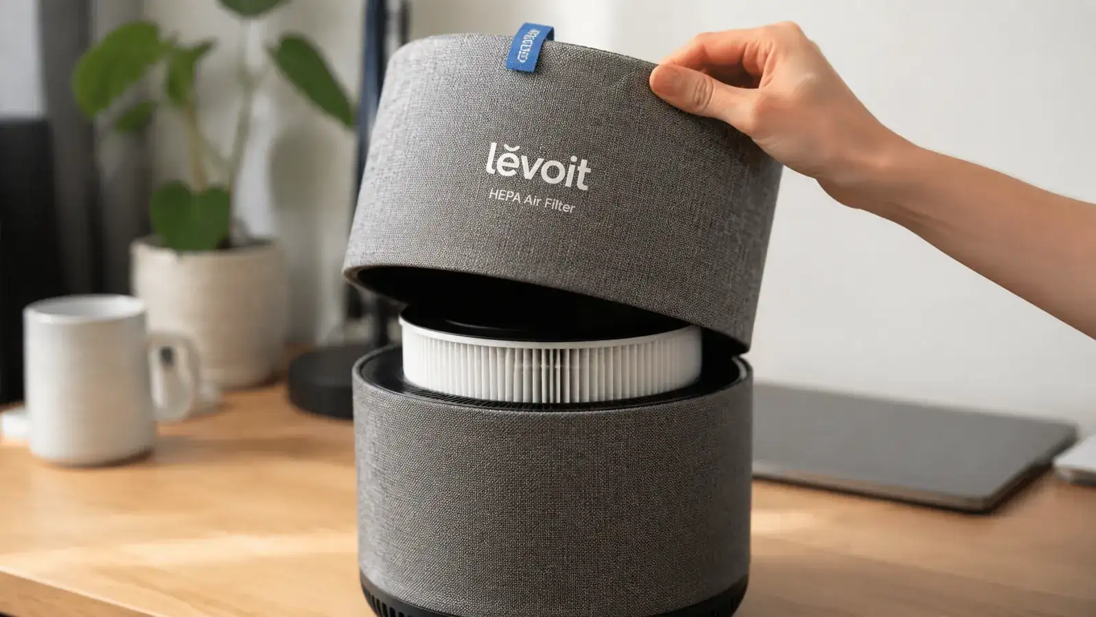 Close-up of a hand lifting the top panel off the LEVOIT air purifier to show the HEPA filter underneath