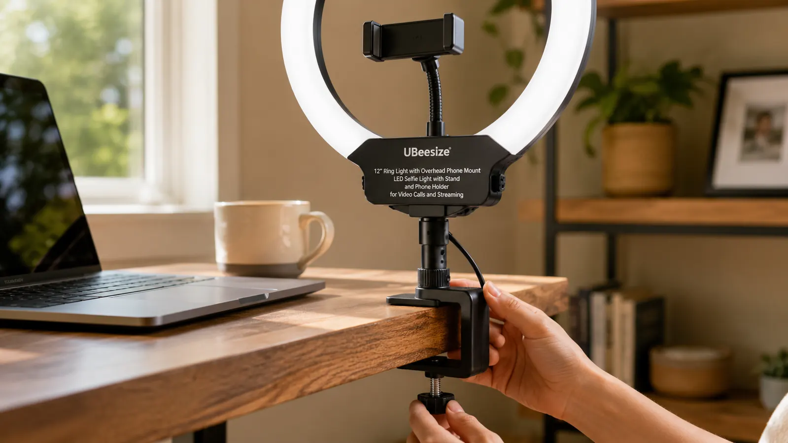 Hand tightening a ring light's desk clamp onto the edge of a wood desk next to a laptop