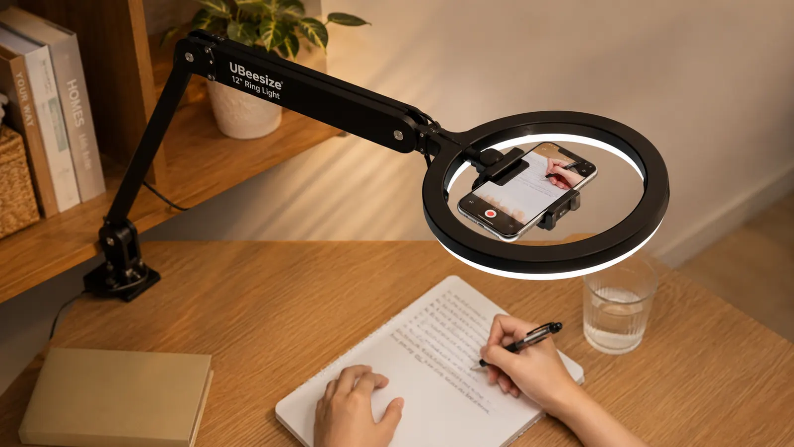 Phone mounted on a ring light's overhead arm recording a desk workspace from above
