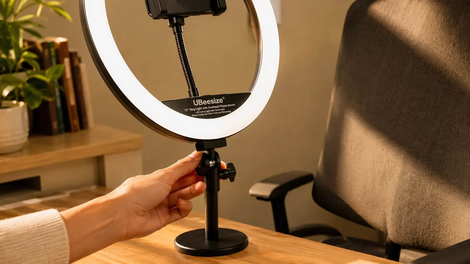 Hand adjusting the tilt of a UBeesize ring light on its desk stand, with the overhead phone mount visible above the ring